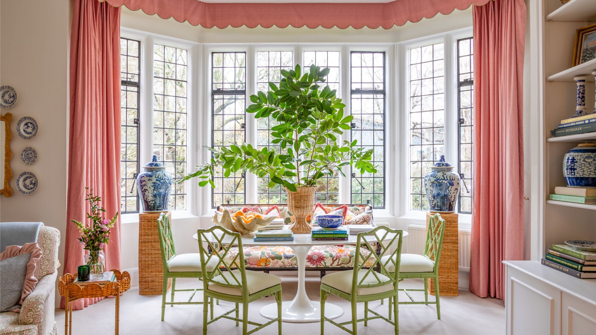 A large sitting room with white walls, coral pink curtains and colourful furniture