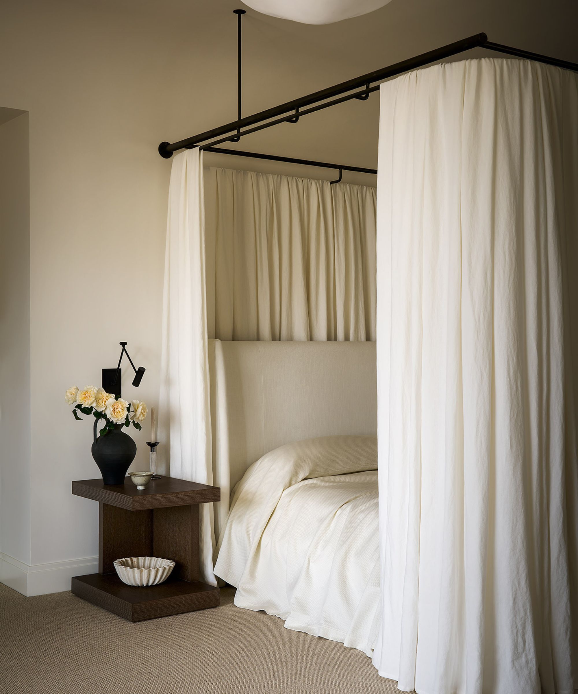 neutral minimalist bedroom with a canopy bed and white bedding, and a dark wooden nightstand