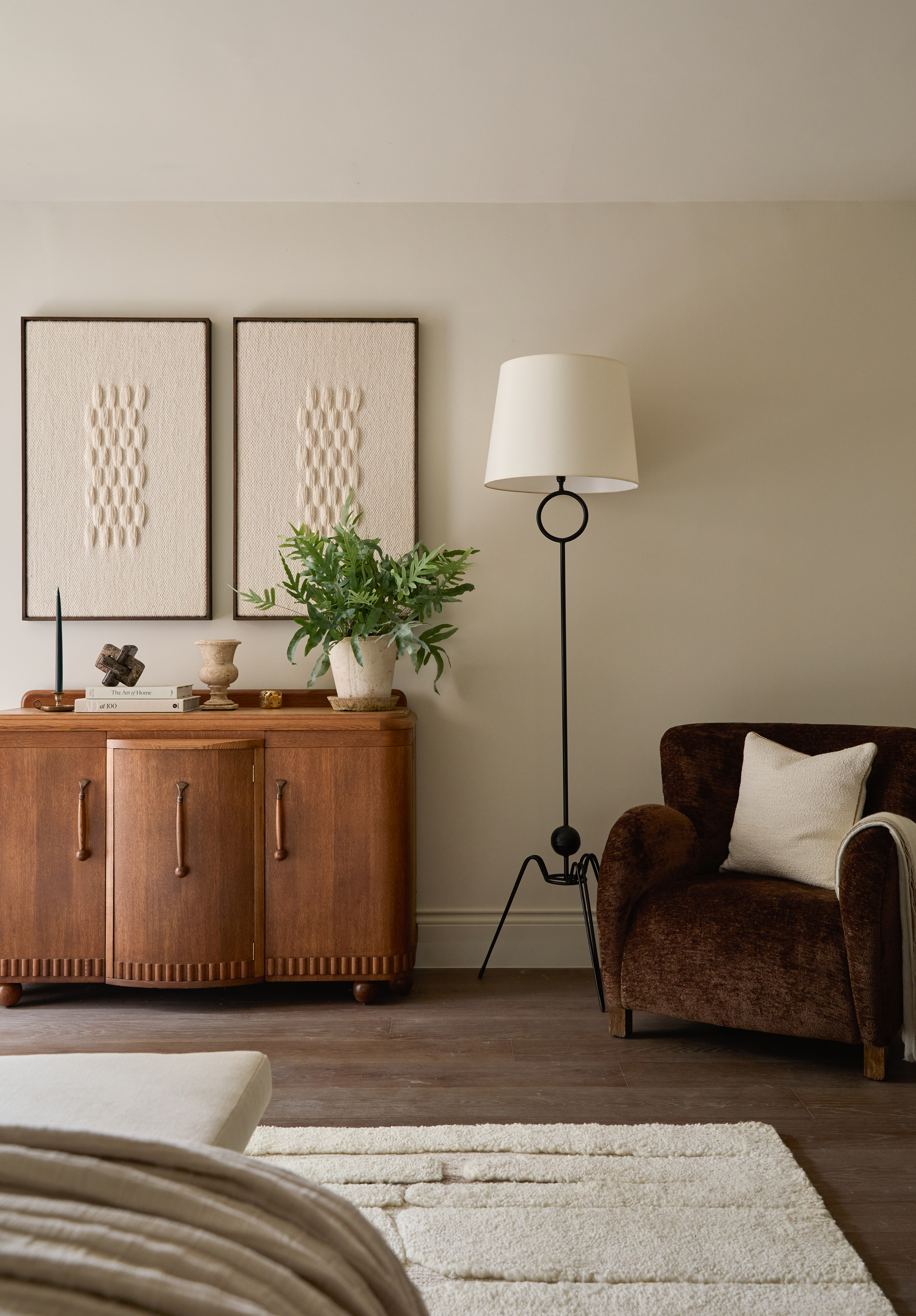 A mic-century style bedroom with a cream rug, a wooden side table, and a brown armchair next to a floorlamp
