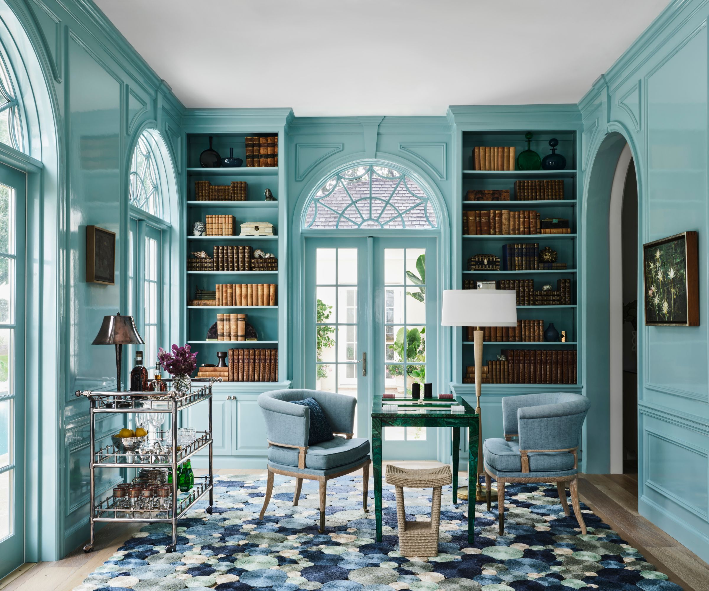 formal library room with light blue color-drenched walls, large glass doors, built-in bookshelves, and blue patterned rug, and two blue armchairs