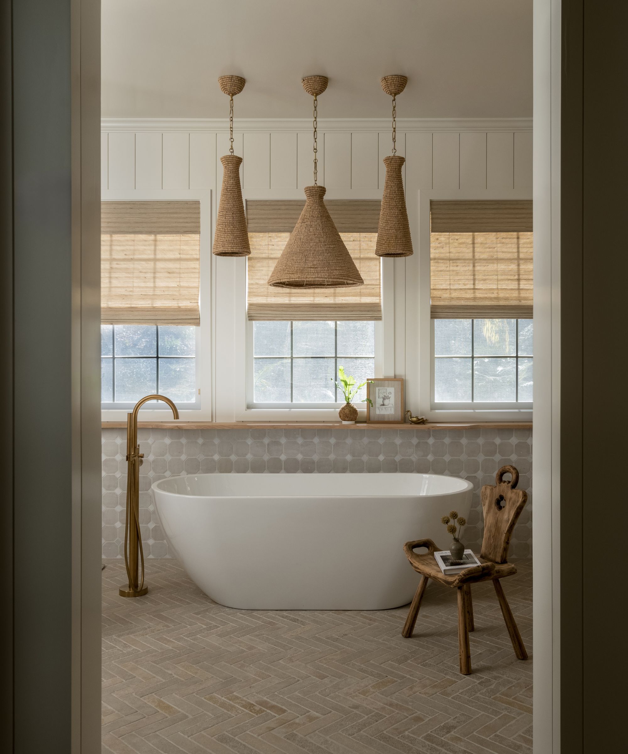 bathroom with neutral color scheme, freestanding bath, woven window blinds, and three rattan pendant lights