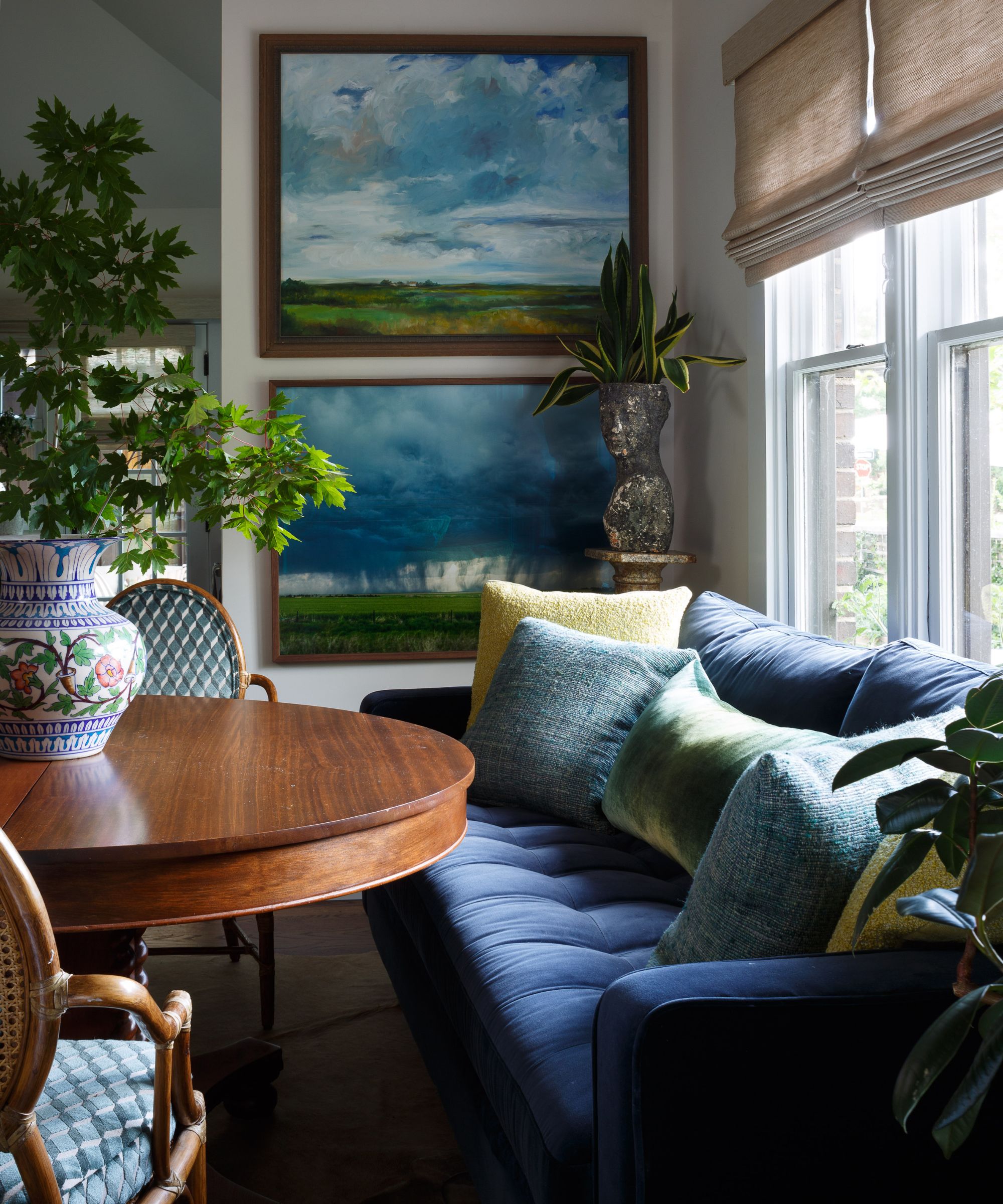 corner of dining area with a dark blue sofa, wooden table, and green and blue artwork and pillows