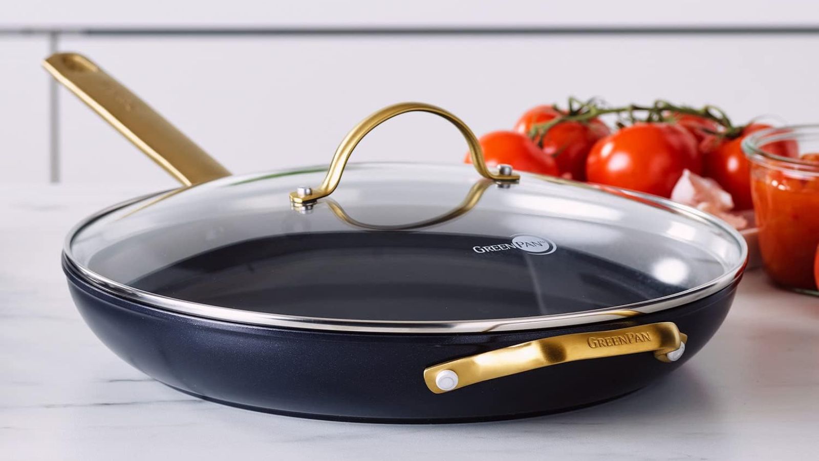 A GreenPan Ceramic Nonstick 12" Frying Pan Skillet with Gold Handle and Lid on a modern counter next to fresh vine tomatoes