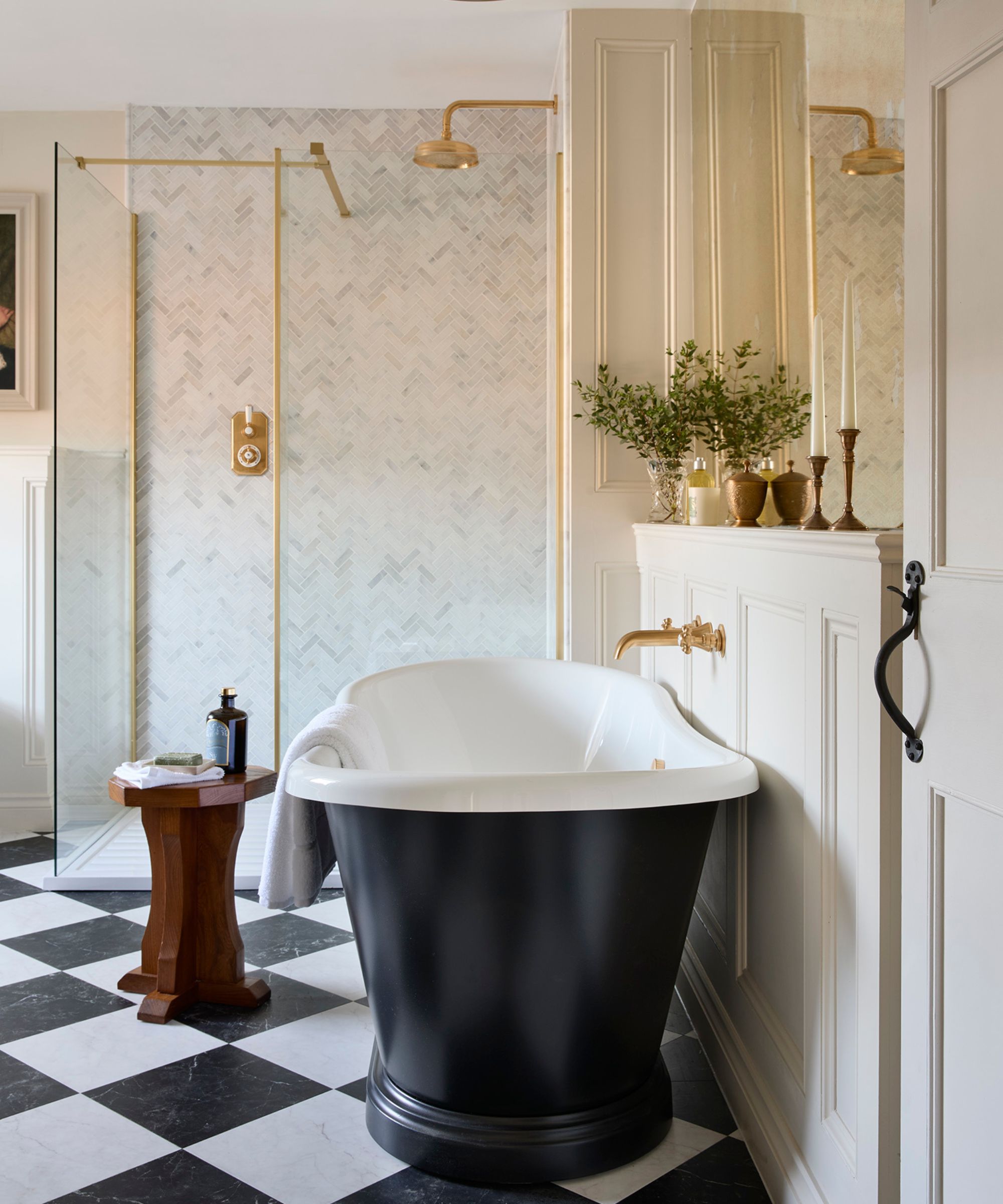 A large bathroom with checkerboard flooring, a freestanding black bath, and a walk-in shower with gold hardware