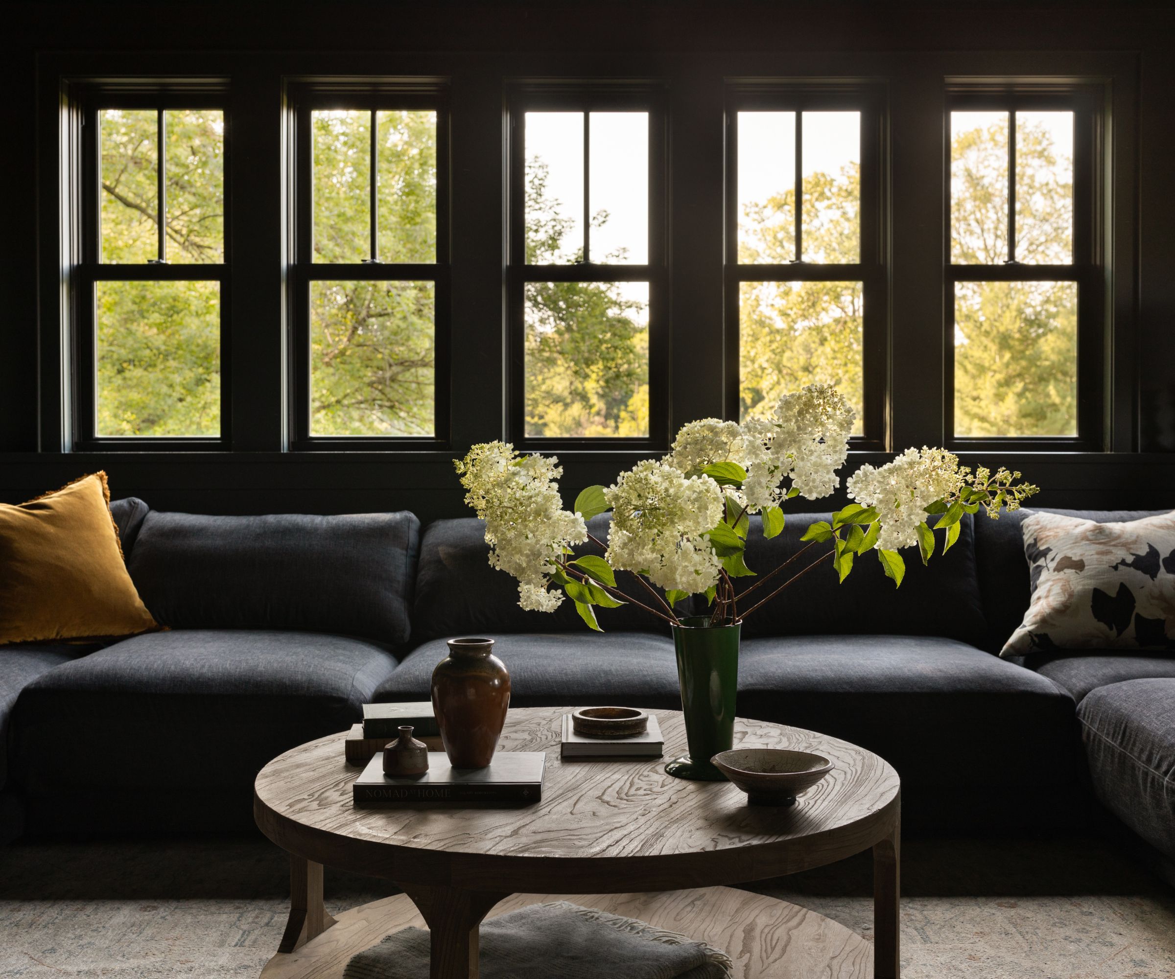 cozy living room with dark blue walls and dark blue sofa, wooden coffee table with a vase of flowers